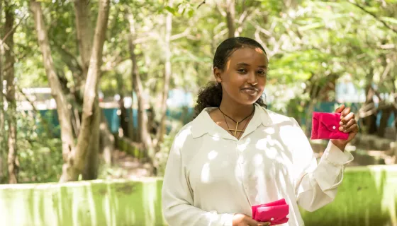 Girl in outdoor space, wearing white shirt and holding pink evenlopes