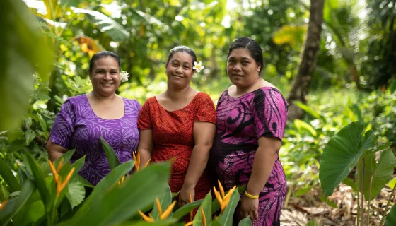 Three women wearing patterned dresses smiling at the camera while standing in a green area