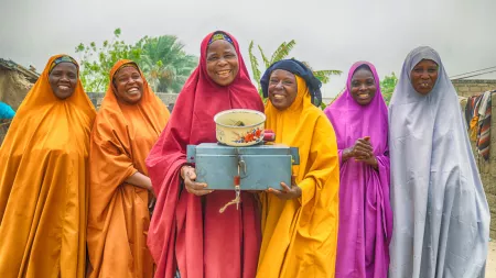 Group of women wearing colorful long vests similiat the camera. The women in the forefront are holding a metal box.