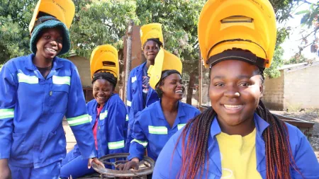 Girls smiling wearing blue work jumpsuits and lifted yellow shielding masks