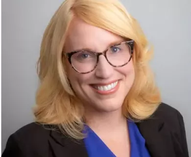 Portrait of blonde woman smiling the camer, wearing glasses, blue shirt and black jacket