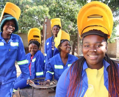 Girls smiling wearing blue work jumpsuits and lifted yellow shielding masks